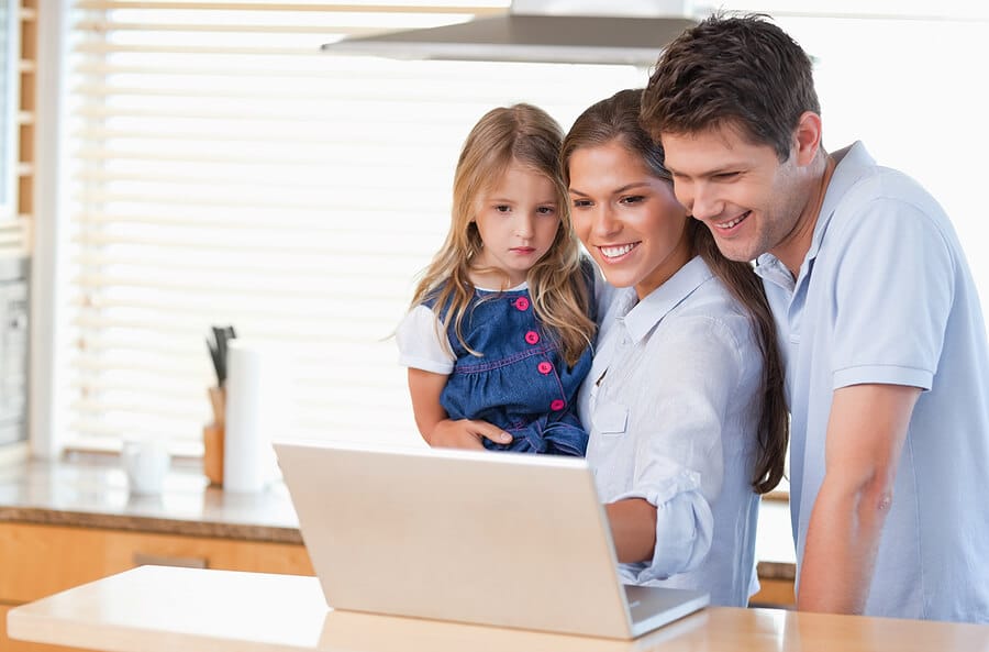 Vater, Mutter und Tochter schauen in der Küche auf einen Laptop