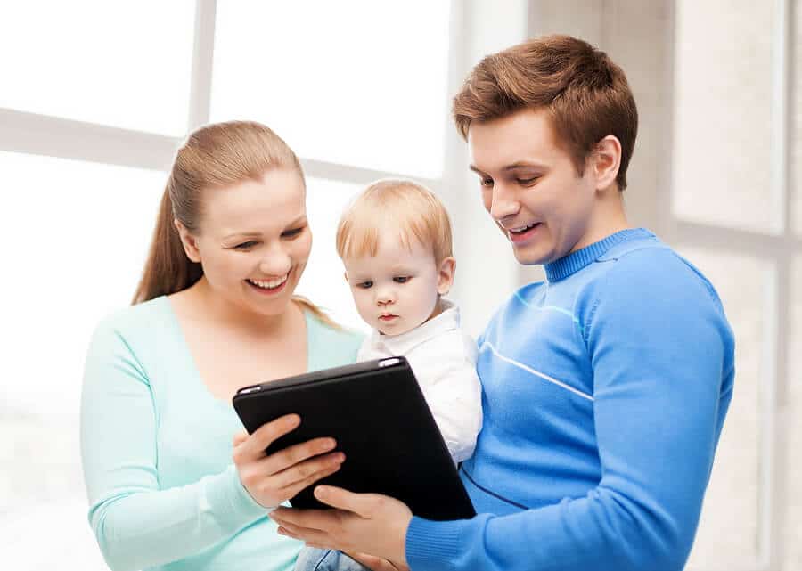 Junge Eltern mit Kind schauen auf ein Tablet und lachen